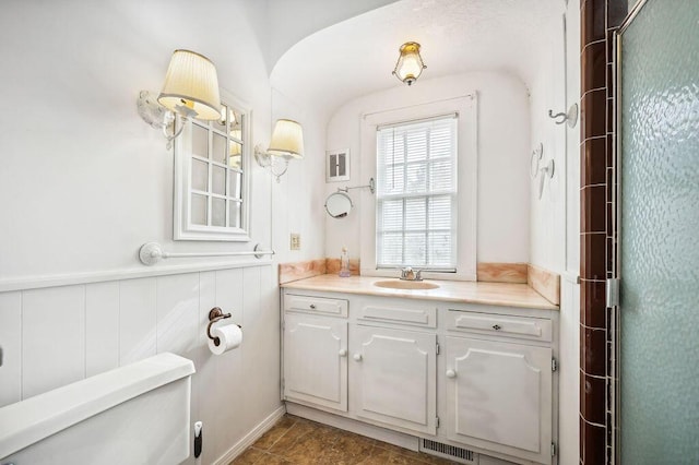 bathroom with toilet, vanity, wainscoting, and visible vents