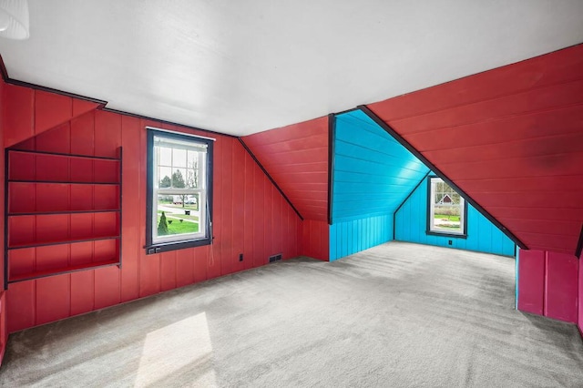 bonus room with carpet flooring, lofted ceiling, wood walls, and a healthy amount of sunlight