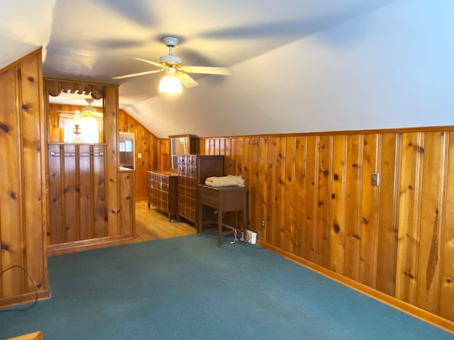 home office with wood walls, a ceiling fan, carpet flooring, and vaulted ceiling