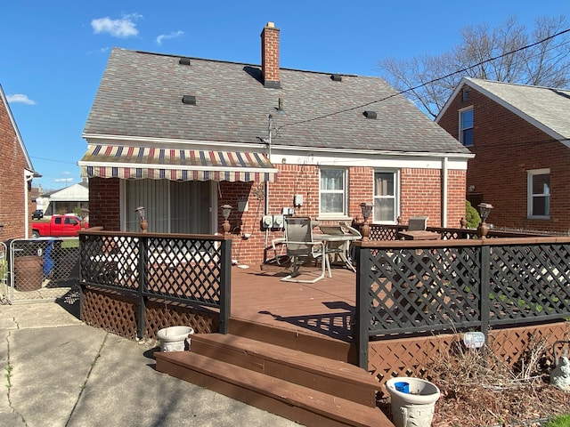 rear view of house featuring a deck, a chimney, brick siding, a shingled roof, and outdoor dining space