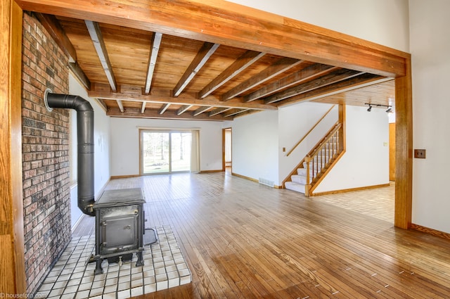unfurnished living room featuring a wood stove, wooden ceiling, beam ceiling, baseboards, and hardwood / wood-style flooring