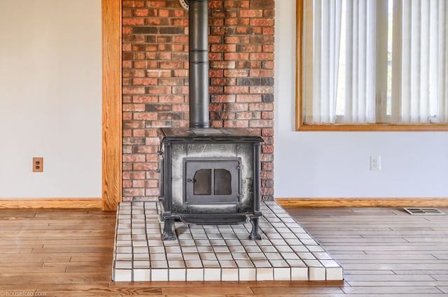 details with visible vents, wood finished floors, baseboards, and a wood stove