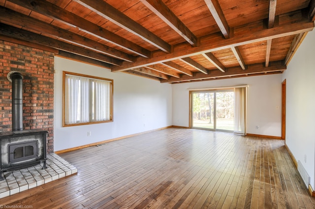 unfurnished living room with beamed ceiling, baseboards, a wood stove, and wood-type flooring