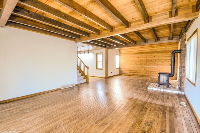 unfurnished living room with hardwood / wood-style floors, a wood stove, beamed ceiling, wooden ceiling, and visible vents