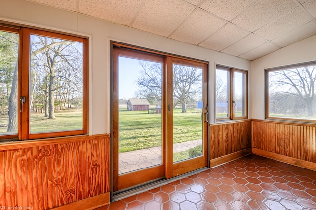 unfurnished sunroom with tile patterned flooring, a wainscoted wall, and wooden walls