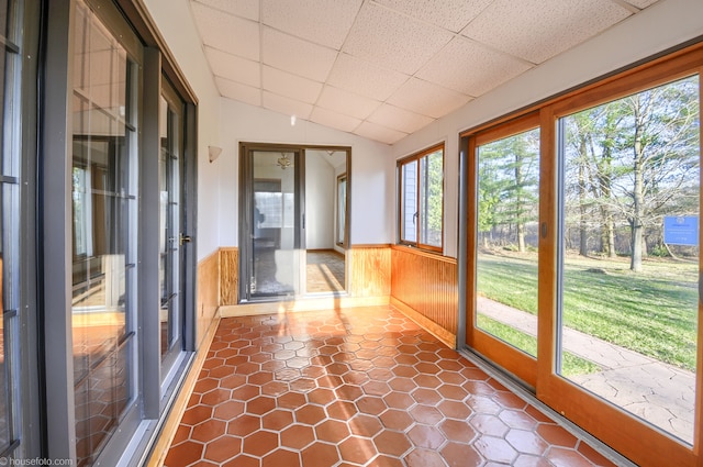 unfurnished sunroom with lofted ceiling, a healthy amount of sunlight, a drop ceiling, and wainscoting