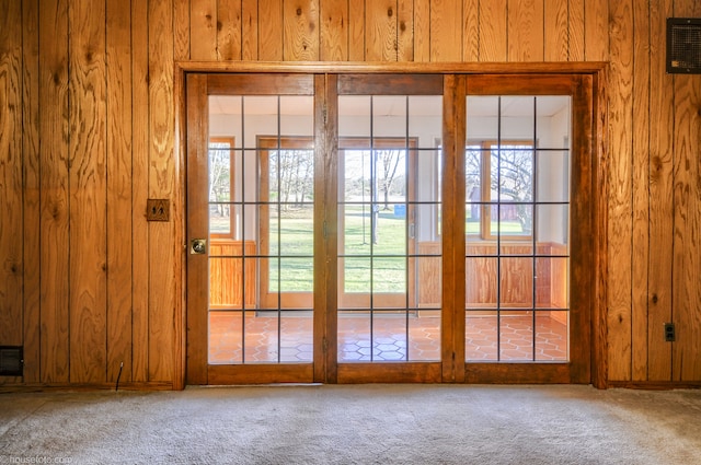 doorway with plenty of natural light, wooden walls, and carpet