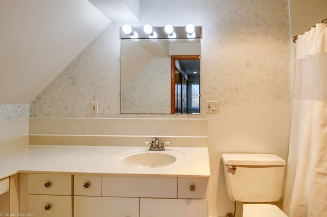full bathroom with vaulted ceiling, toilet, vanity, and wallpapered walls
