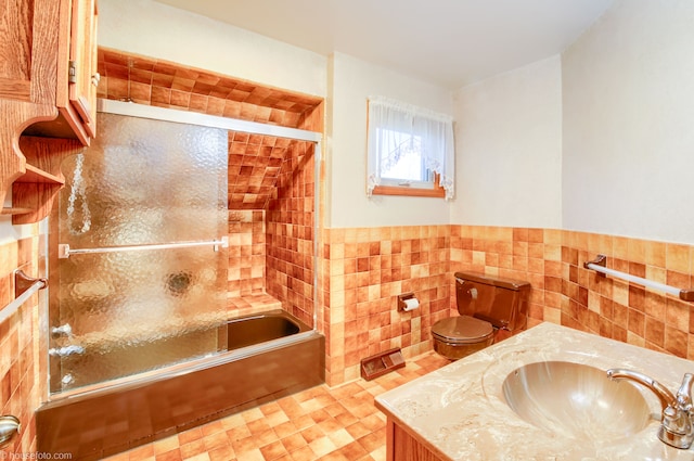 full bathroom featuring tile walls, combined bath / shower with glass door, wainscoting, and vanity