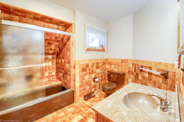 full bath with a wainscoted wall, toilet, vanity, tile walls, and bath / shower combo with glass door