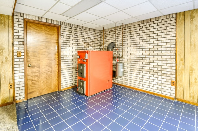 interior space with brick wall, dark tile patterned floors, and a drop ceiling