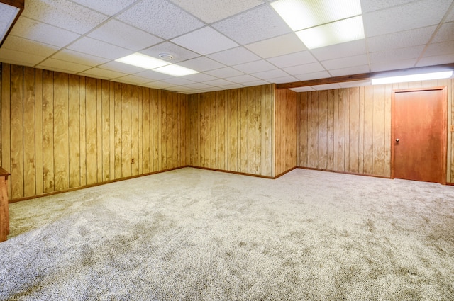carpeted spare room with a drop ceiling, baseboards, and wood walls