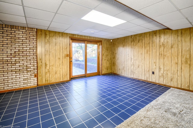 empty room featuring wooden walls, a paneled ceiling, tile patterned flooring, and baseboards