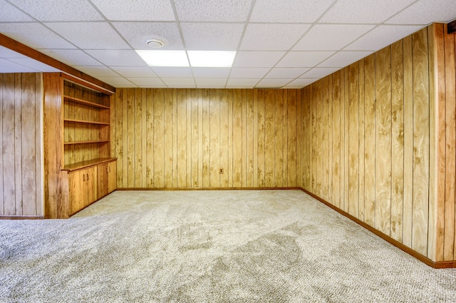 carpeted spare room with a drop ceiling, baseboards, wood walls, and built in features