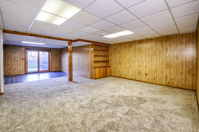 interior space featuring carpet floors, wood walls, a paneled ceiling, and baseboards
