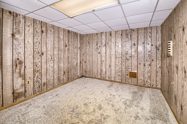 spare room featuring a paneled ceiling, wood walls, and carpet floors