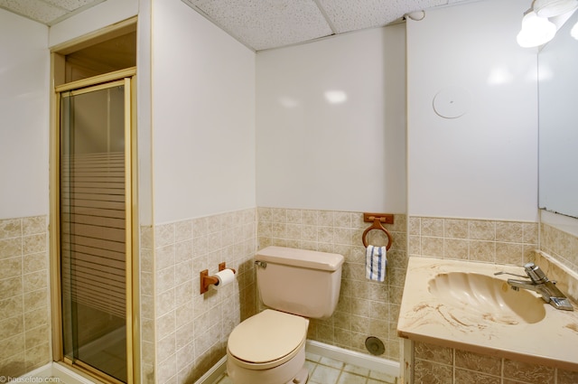 bathroom with a paneled ceiling, toilet, wainscoting, tile walls, and a shower stall