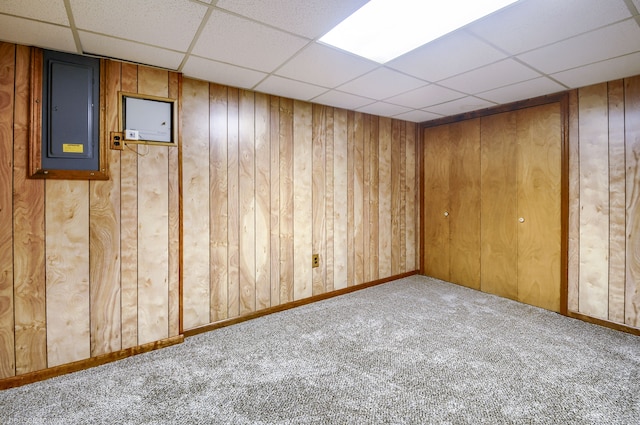 carpeted empty room with electric panel, a paneled ceiling, and wood walls