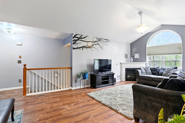 living area with vaulted ceiling, wood finished floors, a glass covered fireplace, and baseboards