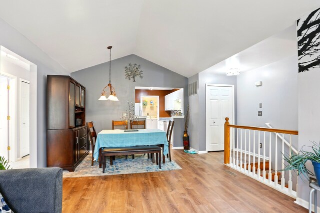 dining room featuring vaulted ceiling, light wood-style flooring, a chandelier, and baseboards