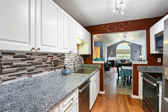 kitchen featuring stainless steel appliances, a sink, light wood finished floors, lofted ceiling, and white cabinets