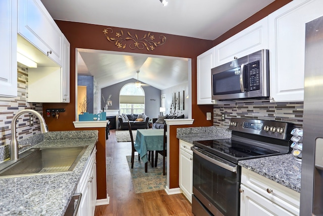 kitchen featuring appliances with stainless steel finishes, a sink, wood finished floors, white cabinetry, and vaulted ceiling