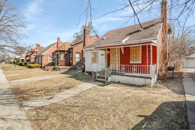 bungalow-style home featuring a porch, a chimney, a residential view, and brick siding