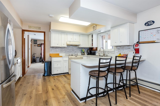 kitchen with a peninsula, freestanding refrigerator, white cabinets, under cabinet range hood, and white range with electric stovetop