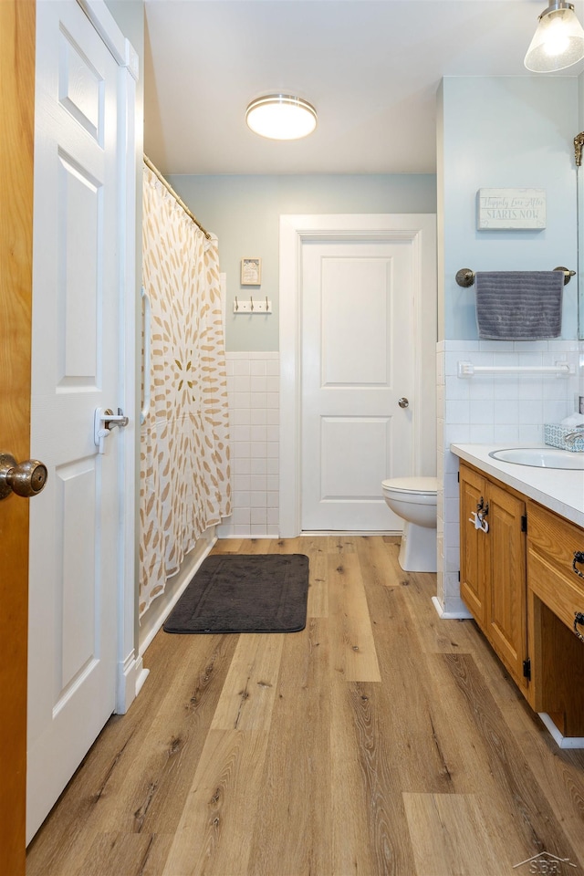 bathroom with toilet, wood finished floors, wainscoting, and tile walls