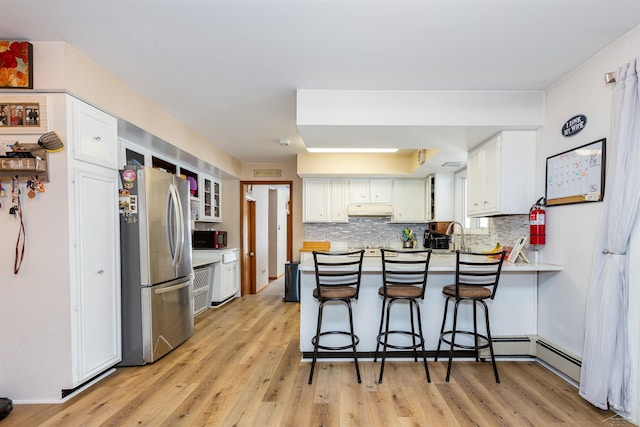 kitchen with a peninsula, light wood-style flooring, white cabinetry, freestanding refrigerator, and decorative backsplash