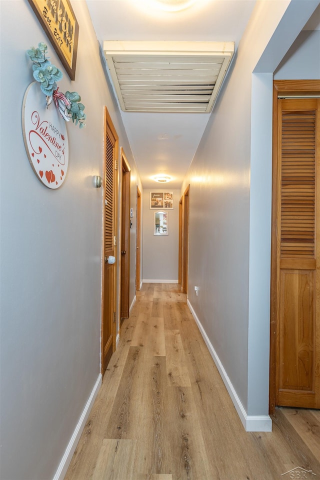 hallway featuring visible vents, baseboards, and light wood finished floors