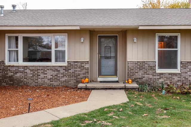 entrance to property with board and batten siding, a shingled roof, and brick siding