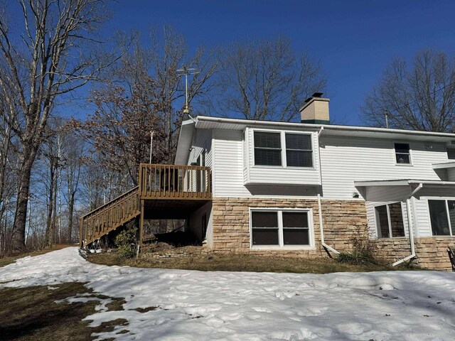 18175 Lake Dr, Big Rapids, MI 49307 - snow covered house featuring a chimney, stone siding, a deck, and stairway