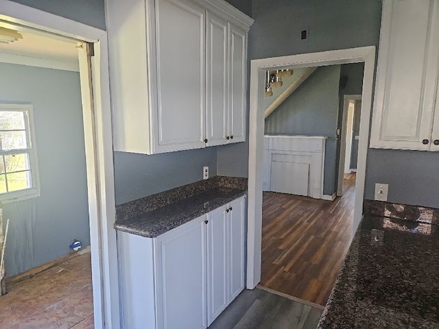 kitchen with dark stone countertops, dark wood-style floors, white cabinetry, and crown molding