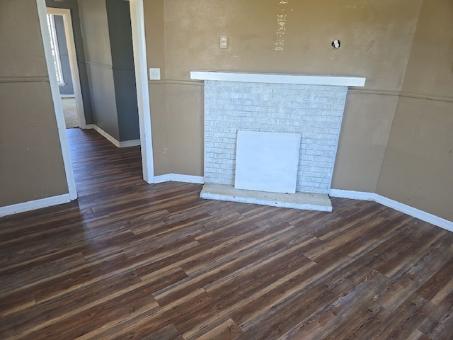 unfurnished living room featuring baseboards, a brick fireplace, and dark wood-style floors