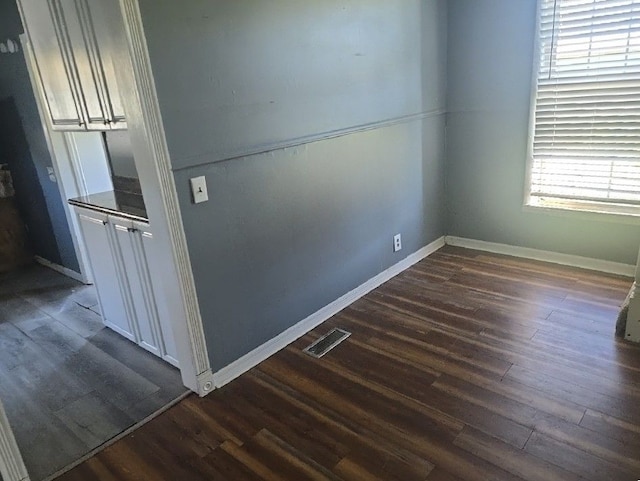empty room with dark wood finished floors, baseboards, and visible vents