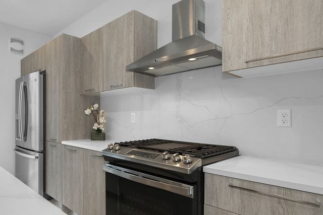 533 E Harrison Ave Unit 29, Royal Oak, MI 48067 - kitchen with light brown cabinetry, modern cabinets, wall chimney exhaust hood, tasteful backsplash, and stainless steel appliances