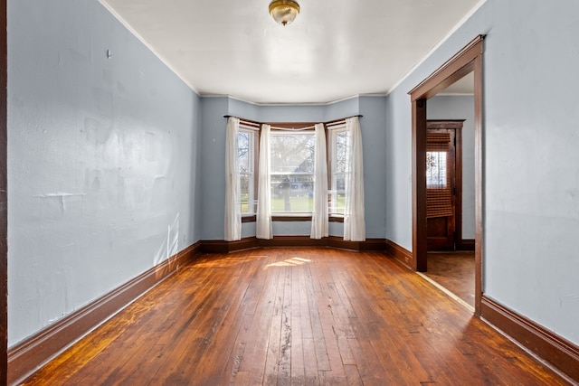 empty room with crown molding, wood-type flooring, and baseboards