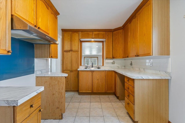 kitchen with brown cabinetry, under cabinet range hood, and backsplash