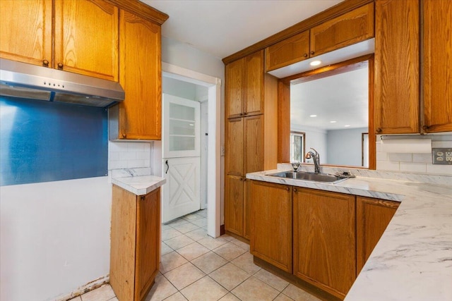 kitchen featuring a sink, light countertops, under cabinet range hood, brown cabinets, and backsplash