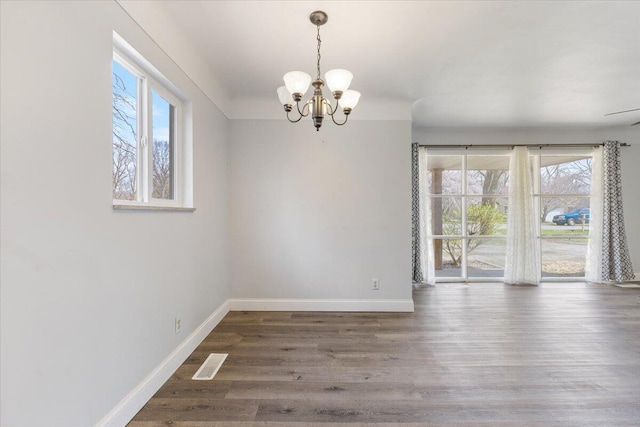 unfurnished dining area featuring baseboards, wood finished floors, a notable chandelier, and visible vents