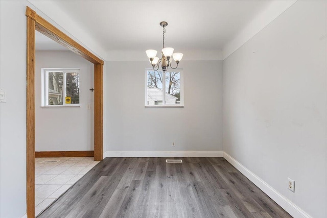 unfurnished dining area with baseboards, a chandelier, wood finished floors, and a healthy amount of sunlight