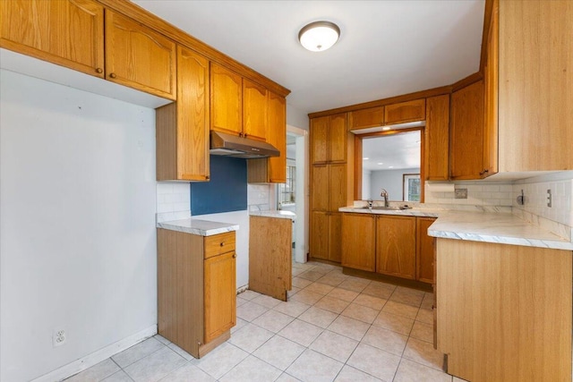 kitchen with under cabinet range hood, tasteful backsplash, a sink, and brown cabinetry