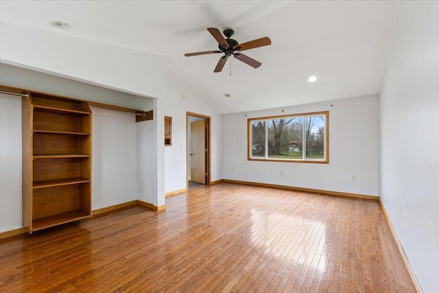 interior space with baseboards, vaulted ceiling, a ceiling fan, multiple closets, and hardwood / wood-style flooring