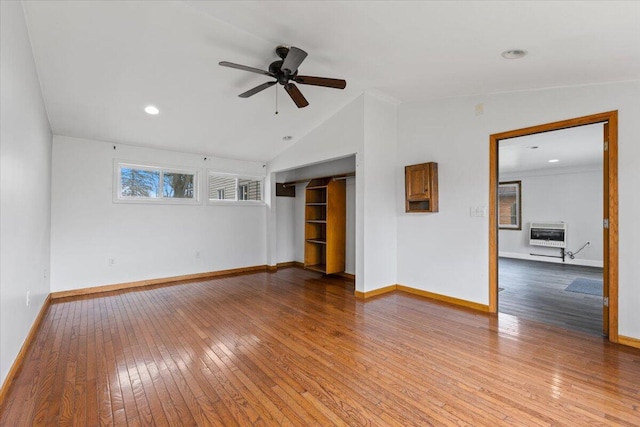 unfurnished living room featuring baseboards, ceiling fan, heating unit, hardwood / wood-style flooring, and vaulted ceiling