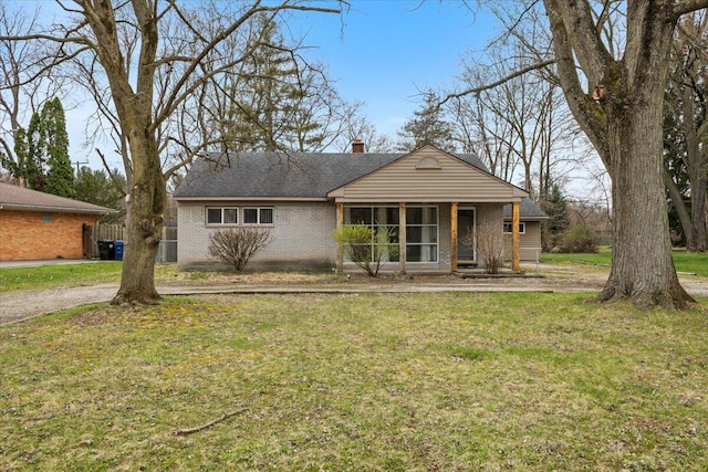 ranch-style home with roof with shingles, a chimney, a front yard, and brick siding