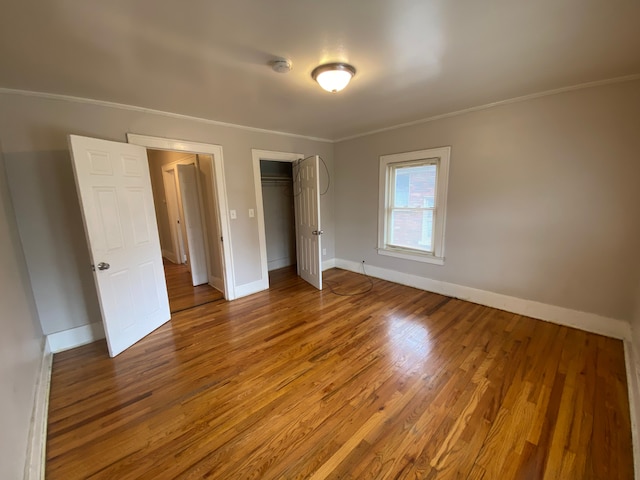 unfurnished bedroom with wood finished floors, a closet, crown molding, and baseboards