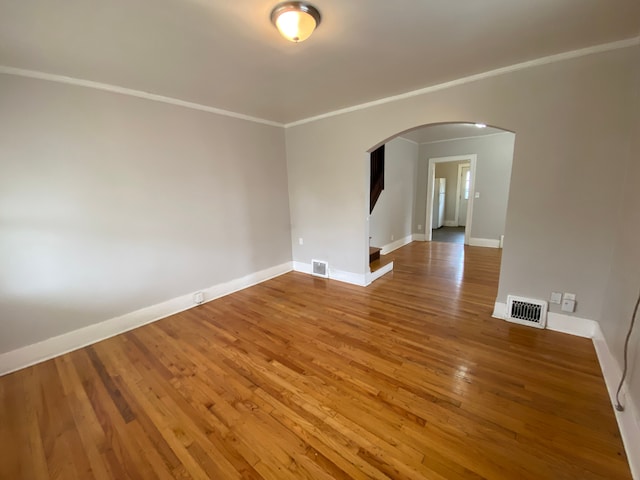 unfurnished room with arched walkways, baseboards, visible vents, wood finished floors, and crown molding
