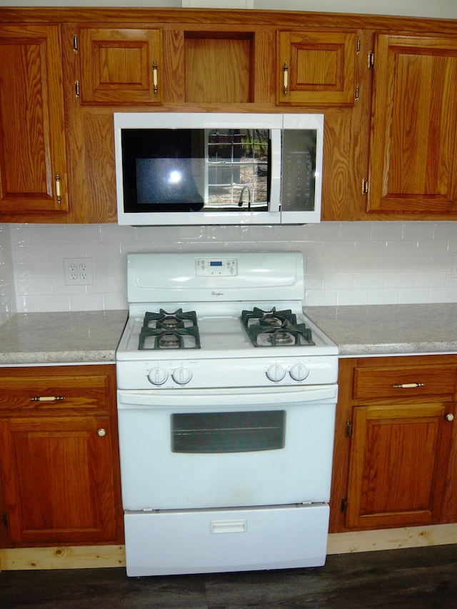kitchen with white gas stove, stainless steel microwave, tasteful backsplash, and brown cabinets