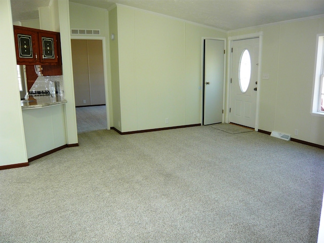 entrance foyer featuring a wealth of natural light, visible vents, light colored carpet, and ornamental molding